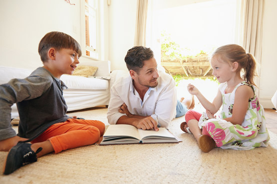 Ein betreuer liest zwei Kindern etwas lustiges und spannendes aus einem Buch vor