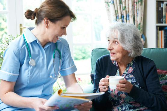 Eine nette Pfleger*in bespricht etwas mit einer älteren Dame, die in einem mintgrünem Sessel sitzt
